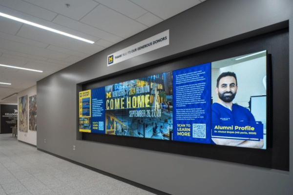 Indoor LED screen displaying alumni profile and event details in a hallway